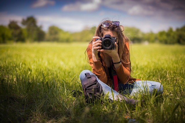 Modelka siedząca na trawie pozuje do zdjęcia z aparatem cyfrowym Nikon